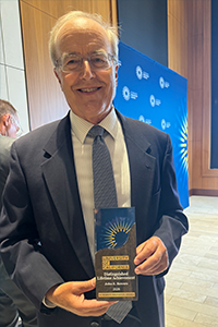 John Bowers smiles while holding his Distinguished Lifetime Achievement Award for Innovation following the University of California awards ceremony.